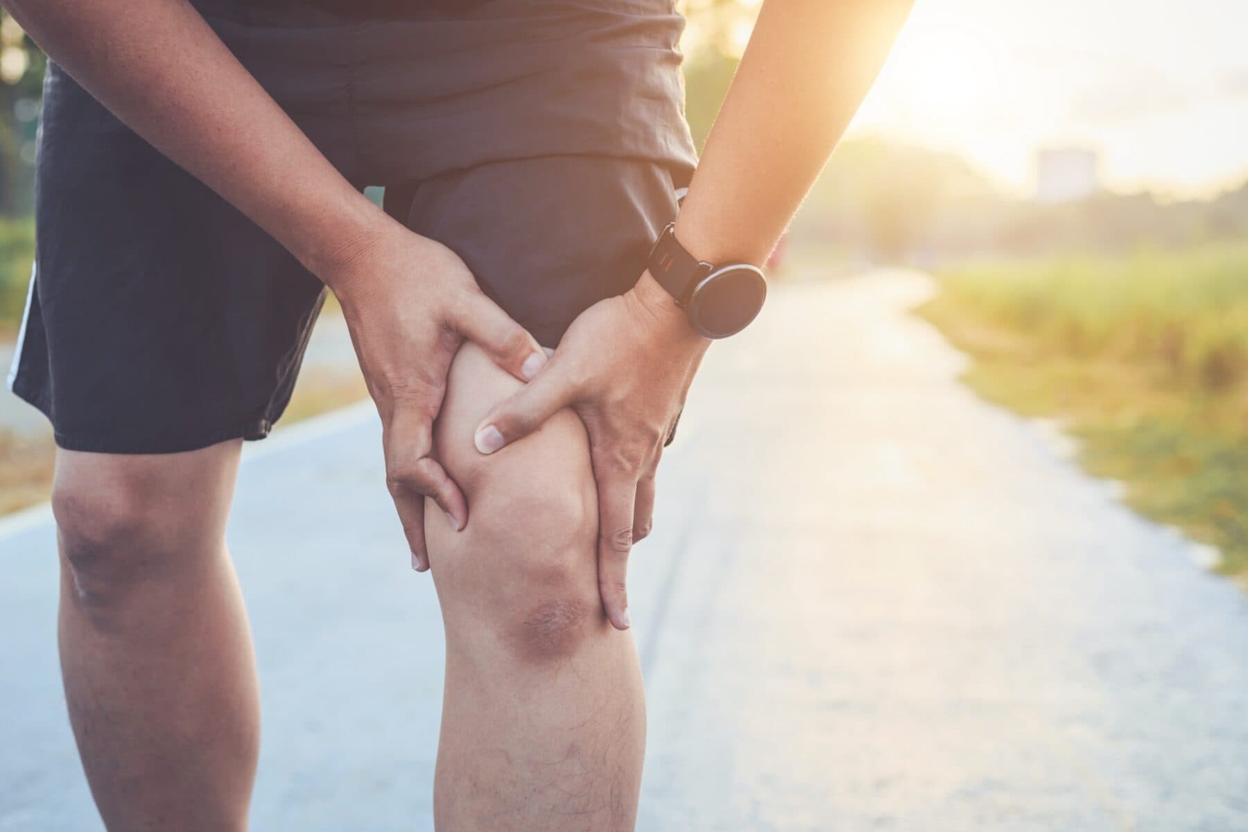 Asian man holding his knee after a run on the road